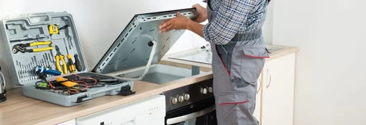 Cooktop repair technician lifting a built-in stovetop for service in Tuscaloosa, AL