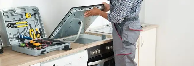 Cooktop repair technician lifting a built-in stovetop for service in Tuscaloosa, AL