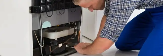 Refrigerator repair technician servicing the compressor and condenser area in Tuscaloosa, AL
