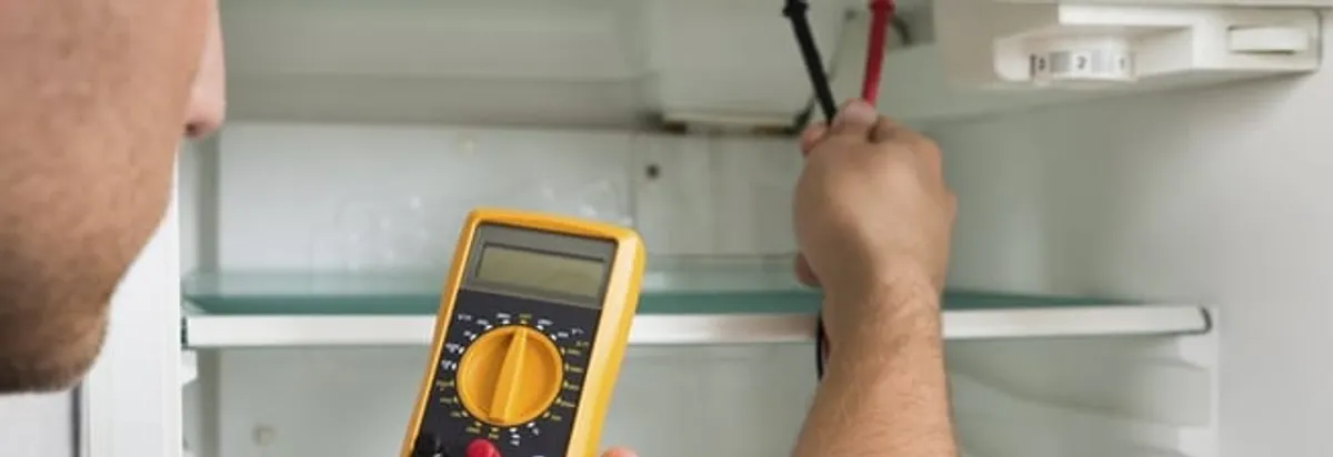 Refrigerator repair technician testing electrical components with a multimeter in Tuscaloosa, AL
