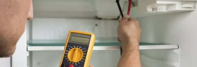 Refrigerator repair technician testing electrical components with a multimeter in Tuscaloosa, AL
