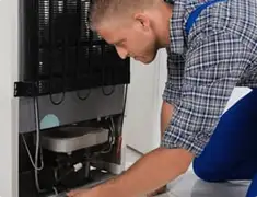 Refrigerator repair technician servicing the compressor and condenser area in Tuscaloosa, AL